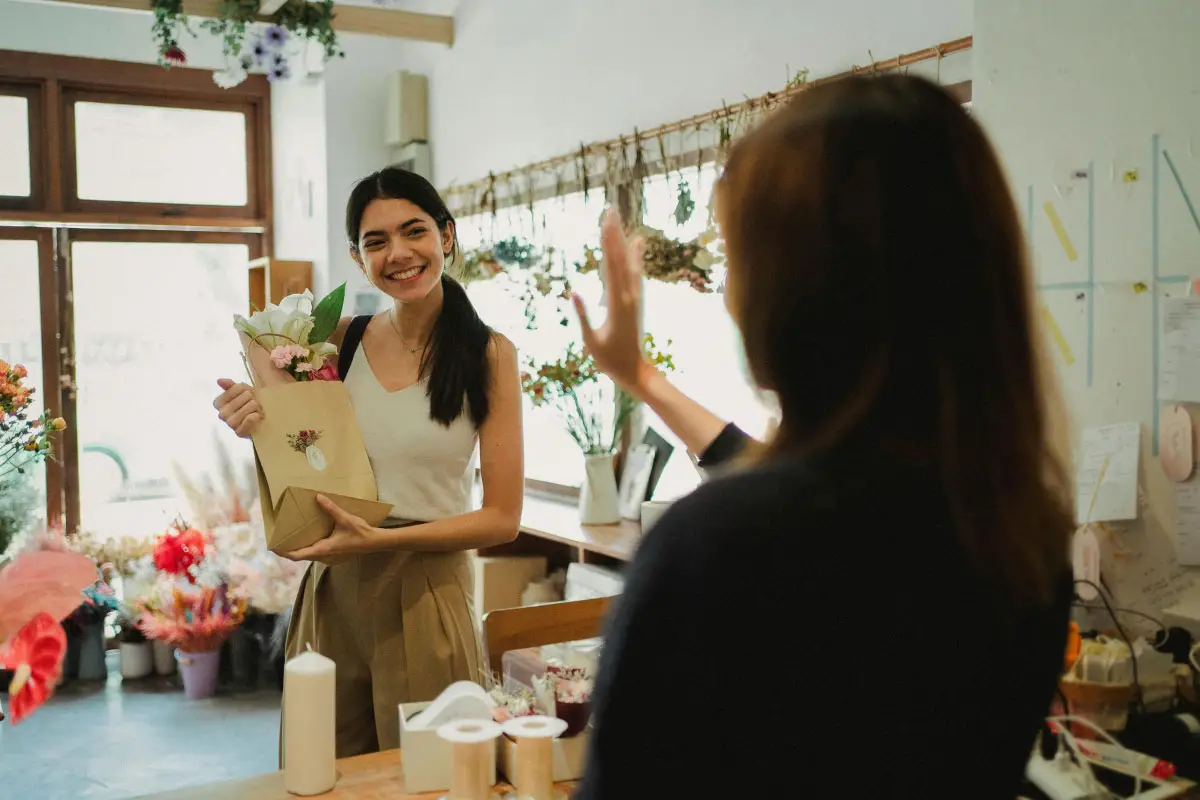 florist owner waves to smiling customer as she leaves her shop