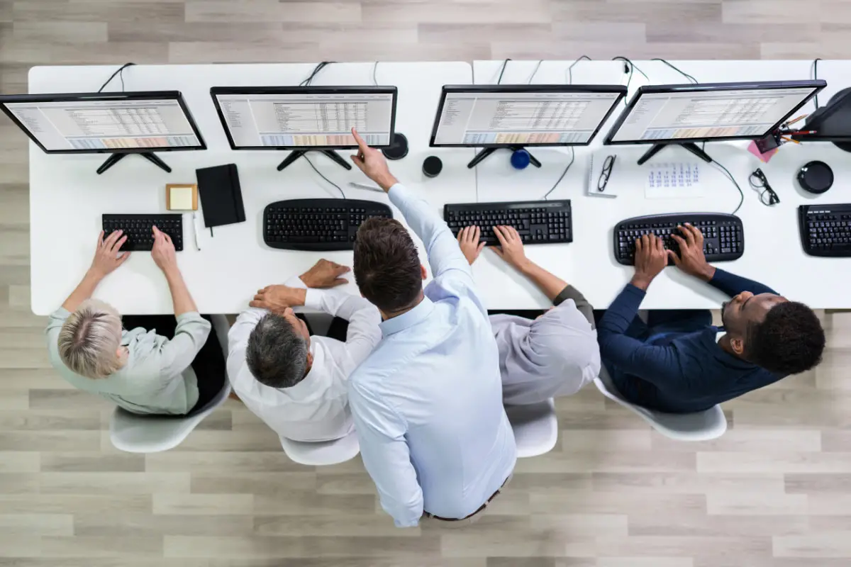 Group of employees seated at computers with a trainer standing behind them and pointing at a monitor during CRM training.