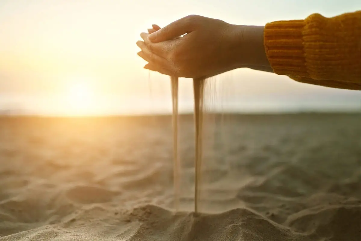 Hands cupping sand on a beach while it pours through the fingers, representing leads being lost over time.